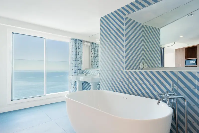 Une baignoire blanche se trouve dans une salle de bain lumineuse avec un mur décoré de motifs bleus et blancs.