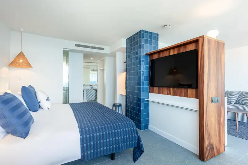 Une chambre lumineuse avec un lit recouvert d'une couverture bleue et un meuble bas en bois.