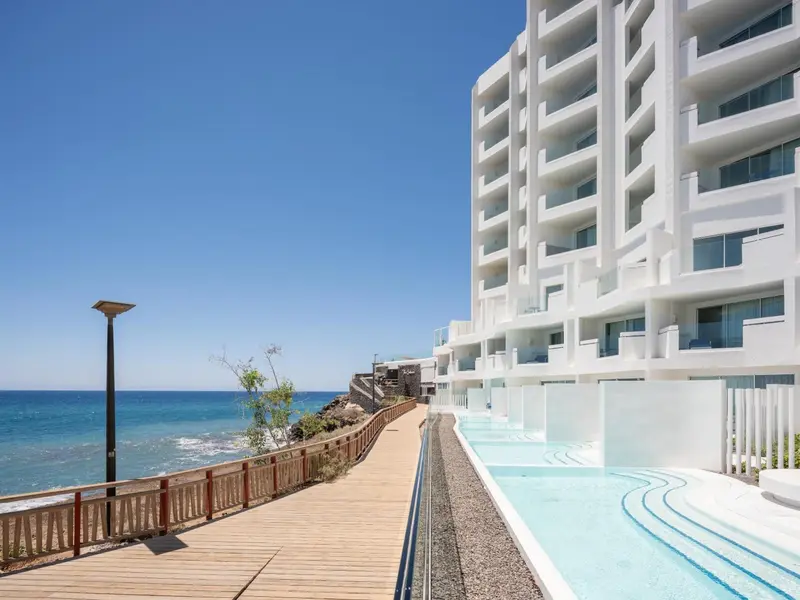 Vue d'un bâtiment blanc moderne avec des balcons surplombant une promenade en bord de mer.