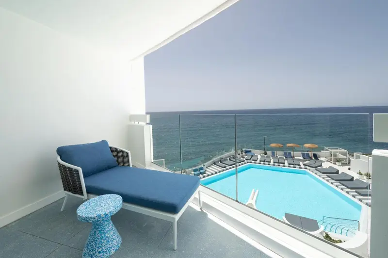 Terrasse avec chaise longue donnant sur une piscine et la mer.