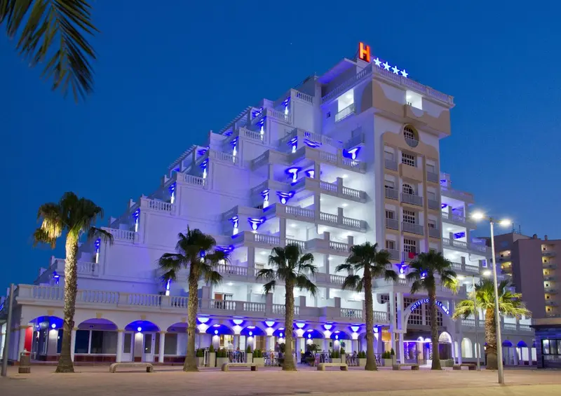 Bâtiment blanc illuminé de bleu avec des palmiers au premier plan.