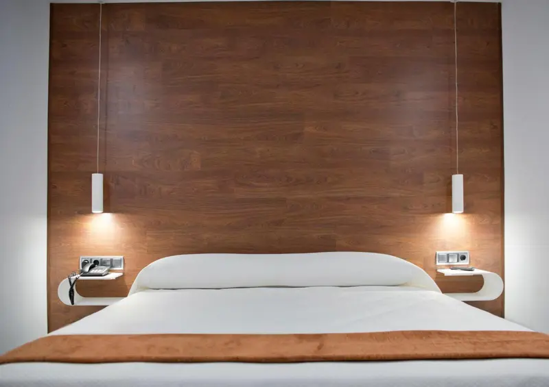 Un lit blanc avec une couverture marron est devant un mur en bois avec des lampes.