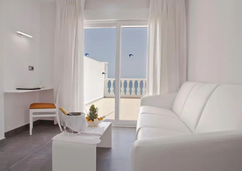 Espace de séjour lumineux avec canapé blanc et accès à un balcon.