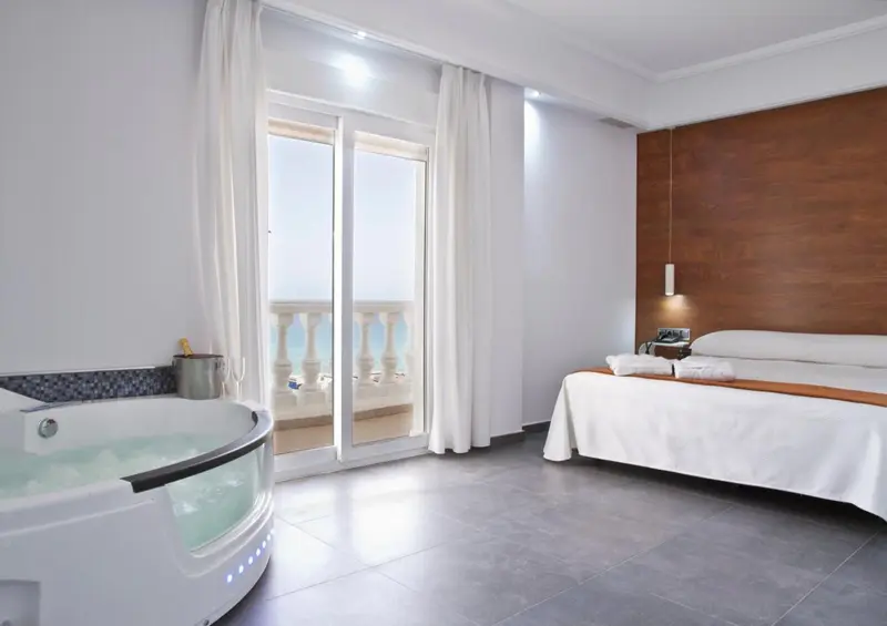 Une chambre lumineuse avec un grand lit et un jacuzzi donnant sur une terrasse.