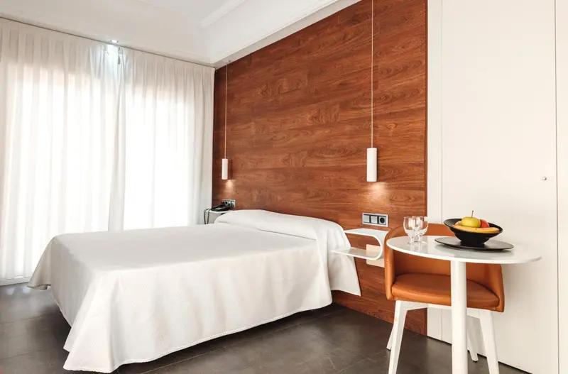 Une chambre lumineuse avec un lit blanc et une petite table.