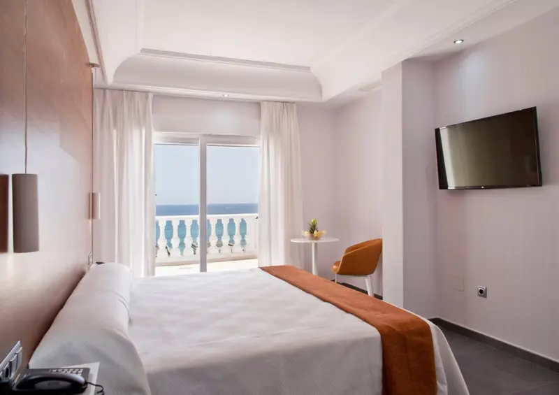 Chambre lumineuse avec un lit fait et une vue sur la mer.