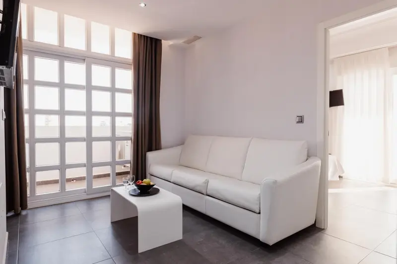 Un salon lumineux avec un canapé blanc et une table basse devant une baie vitrée.