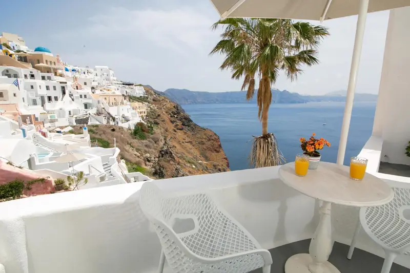 Terrasse avec table et chaises donnant sur une vue panoramique de la mer et des habitations blanches.