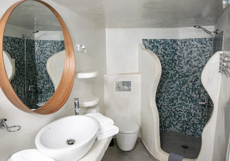 Une salle de bain moderne avec douche à l'italienne et lavabo surmonté d'un grand miroir rond.