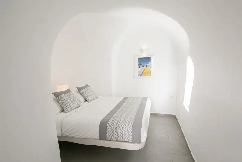 Une chambre lumineuse avec un lit recouvert d'une courtepointe grise et de coussins.