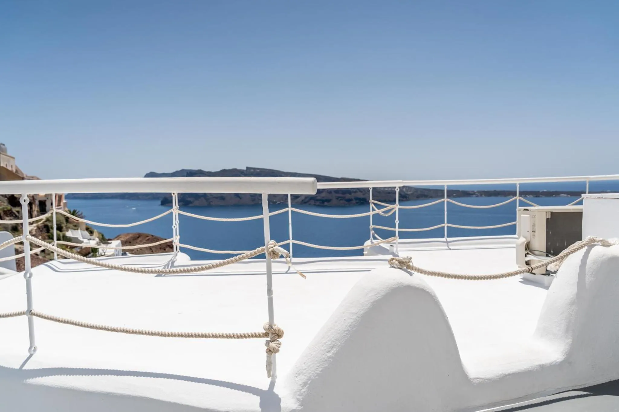 Terrasse blanche avec garde-corps et vue sur la mer bleue et les îles au loin.