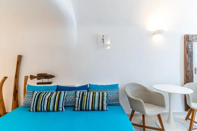Une chambre lumineuse avec un lit turquoise et un fauteuil en rotin.