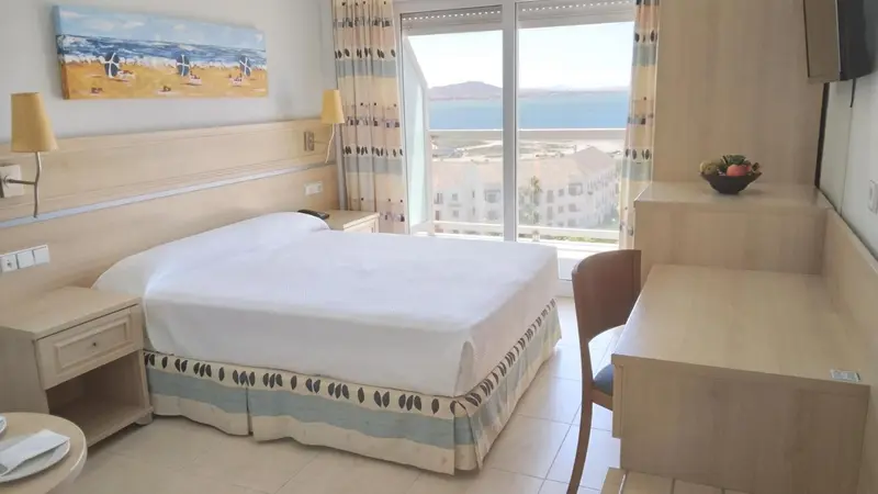 Chambre lumineuse avec un lit blanc et une vue sur la mer.
