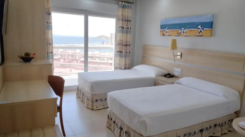 Chambre lumineuse avec deux lits simples et vue sur la mer.