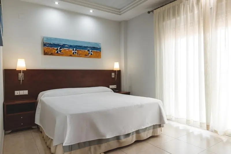 Une chambre lumineuse avec un grand lit recouvert d'une courtepointe blanche.