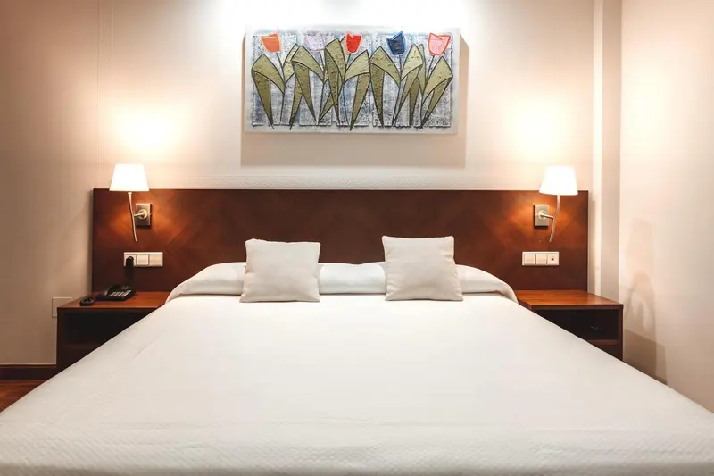 Une chambre lumineuse avec un grand lit blanc et une décoration florale au mur.
