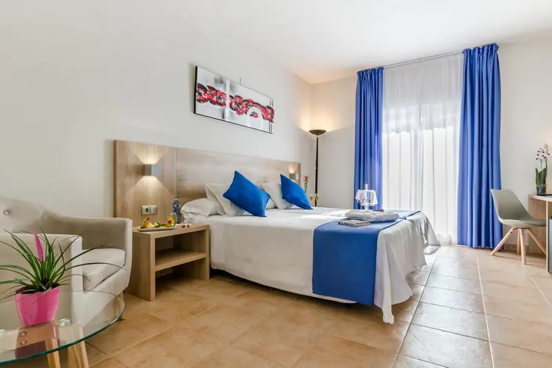 Chambre lumineuse avec un lit double et un fauteuil.