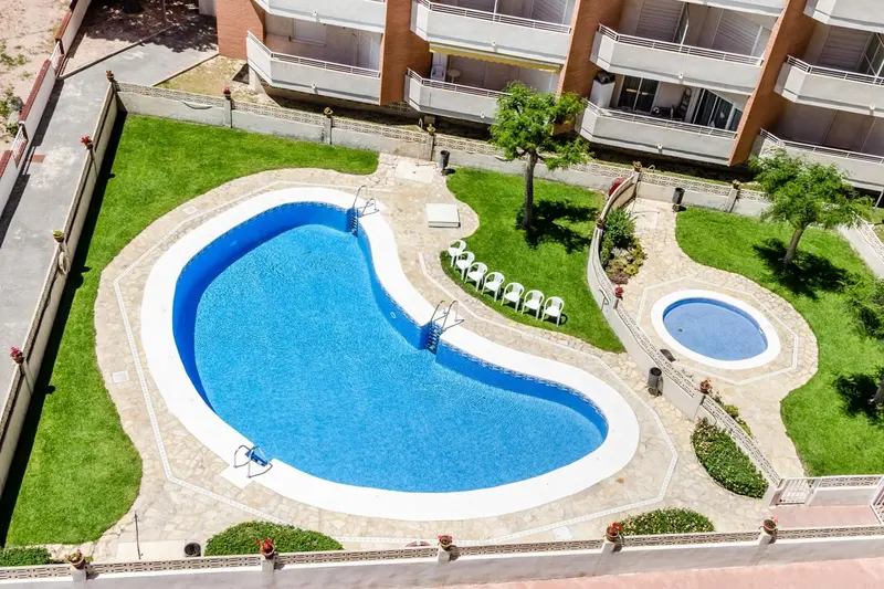 Vue aérienne d'une piscine en forme d'haricot entourée d'une pelouse verdoyante.