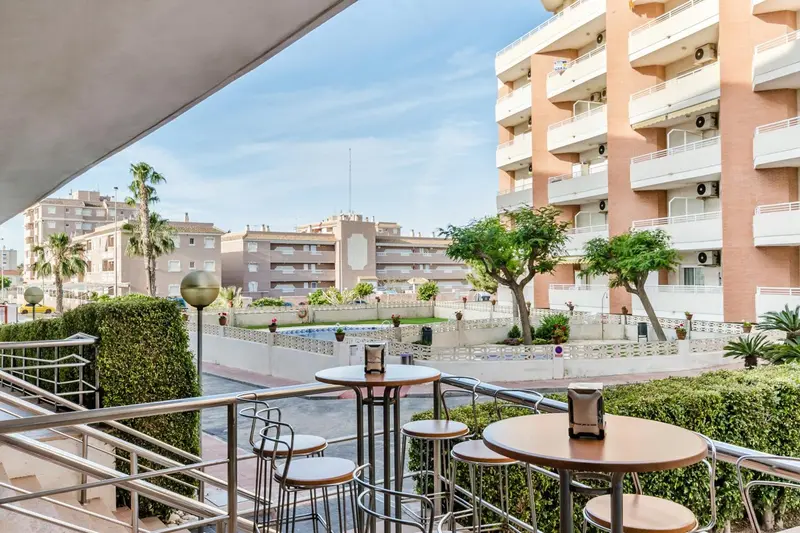 Terrasse avec tables et chaises donnant sur un bâtiment et une végétation luxuriante.