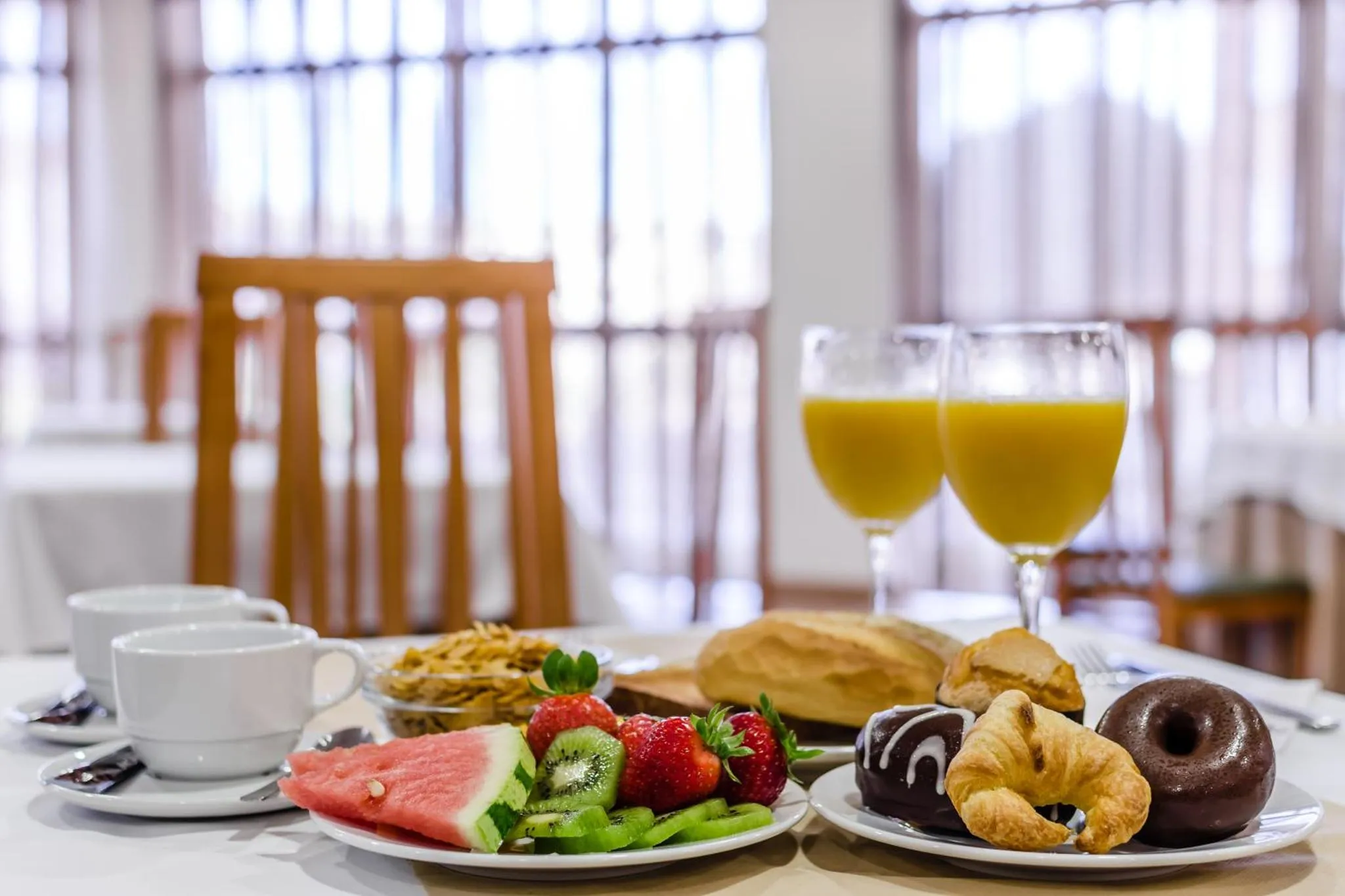 Une table est dressée avec un petit-déjeuner composé de fruits, de viennoiseries et de boissons.