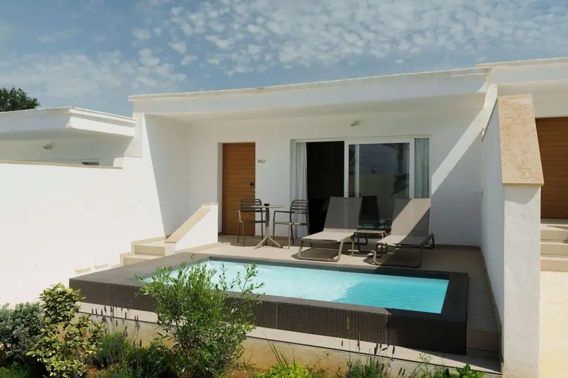 Terrasse privée avec petite piscine devant un logement blanc.