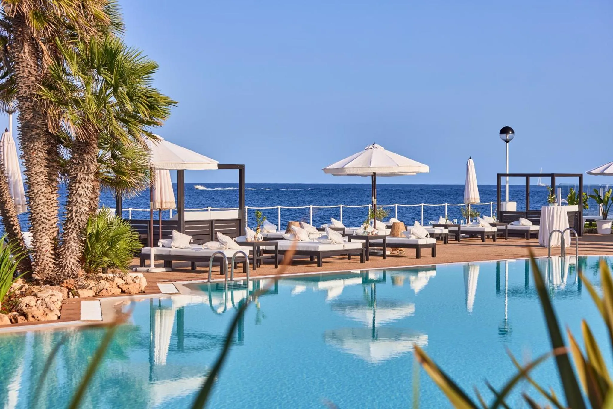 Transats blancs et parasols au bord d'une piscine turquoise avec vue sur la mer.