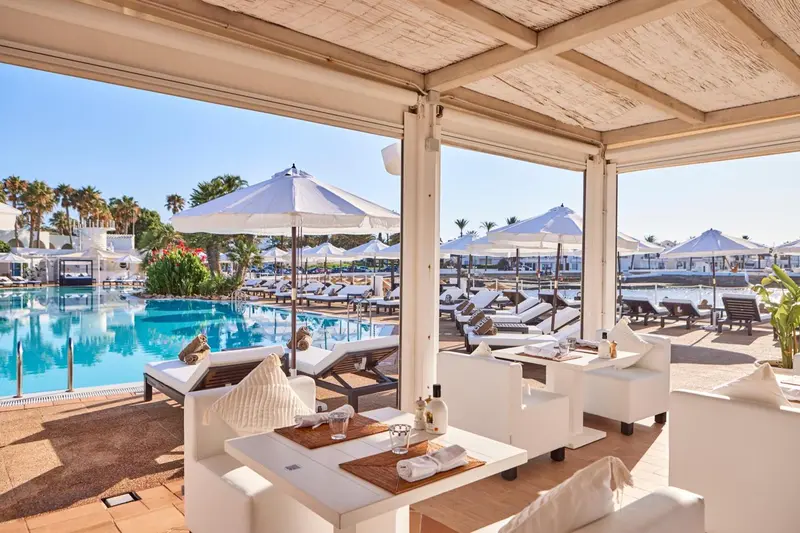 Espace de détente extérieur avec tables et chaises blanches près d'une piscine.
