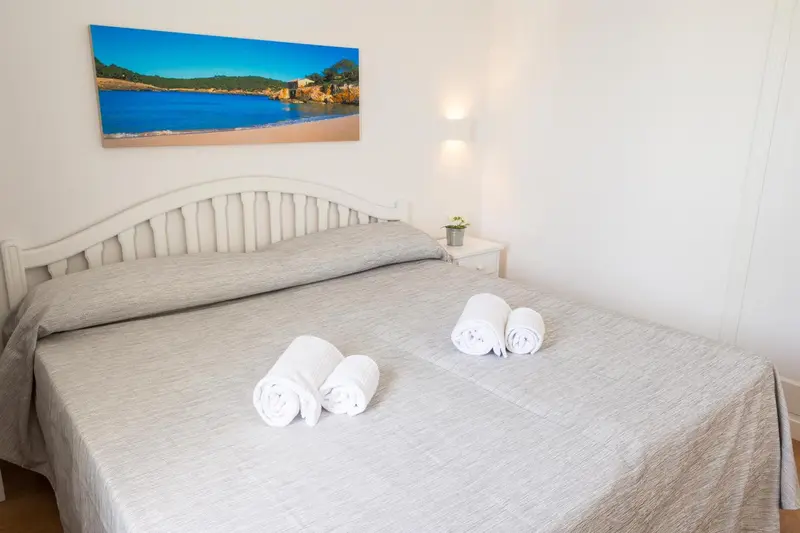 Une chambre lumineuse avec un grand lit recouvert d'une couverture grise et de serviettes enroulées.