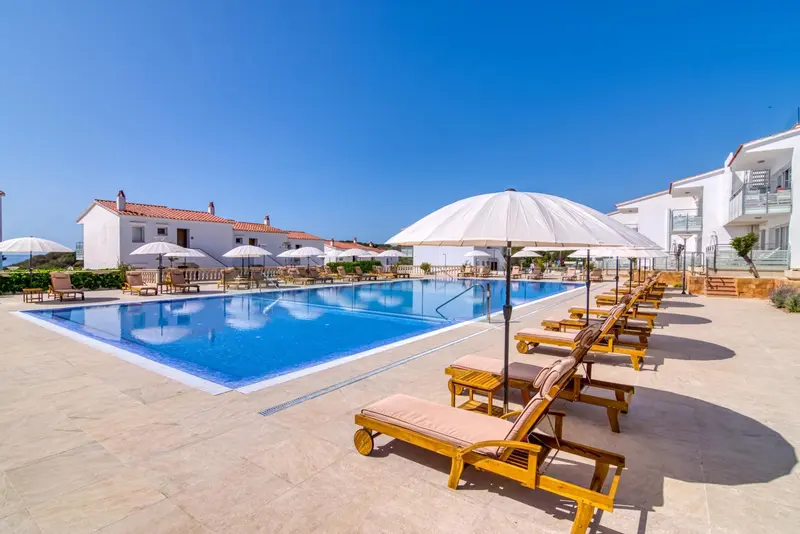 Transats et parasols bordent une piscine rectangulaire dans un complexe hôtelier.