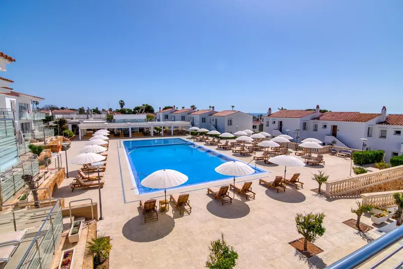 Vue aérienne d'une piscine entourée de transats et de parasols blancs.
