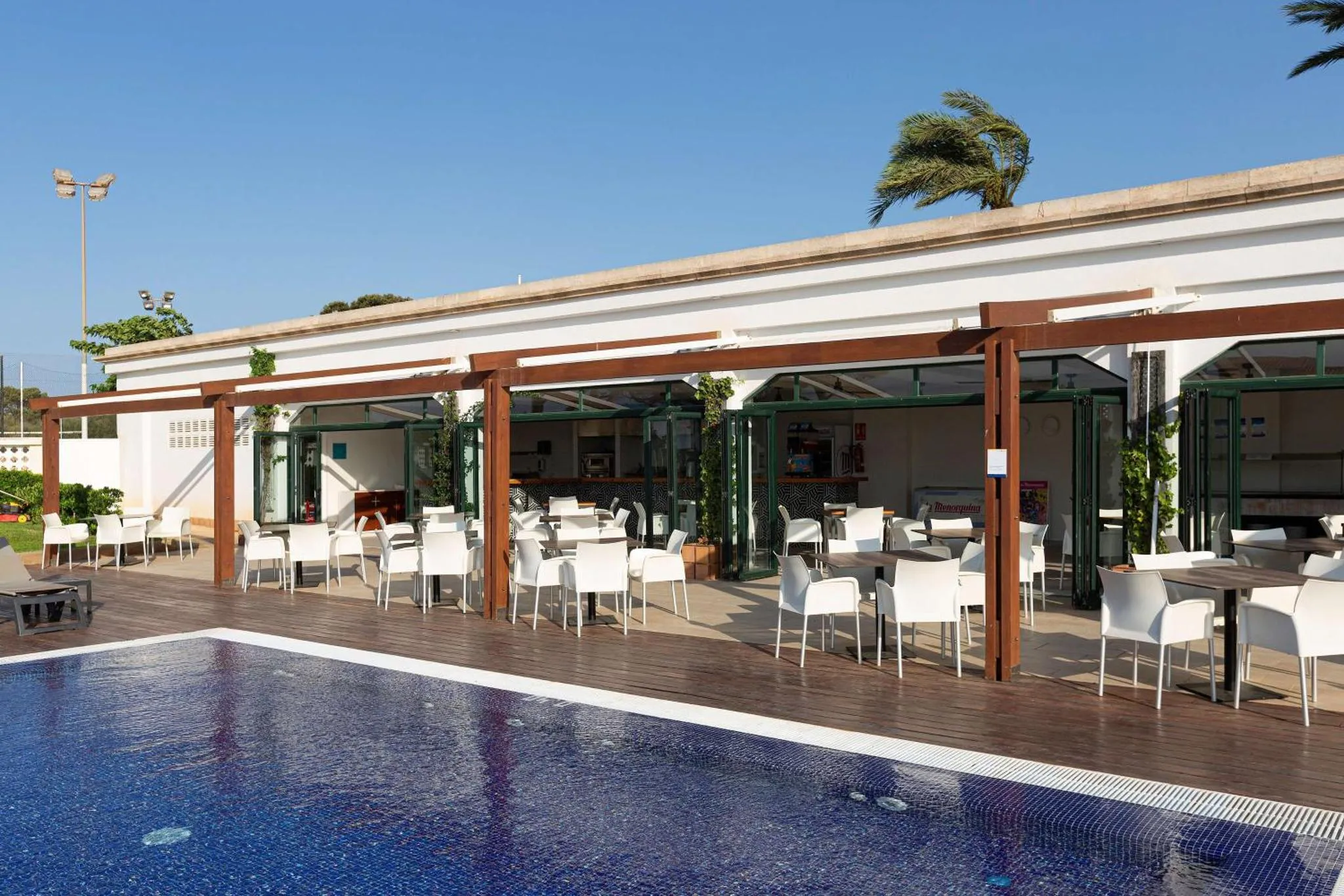 Terrasse ombragée avec tables et chaises près d'une piscine.