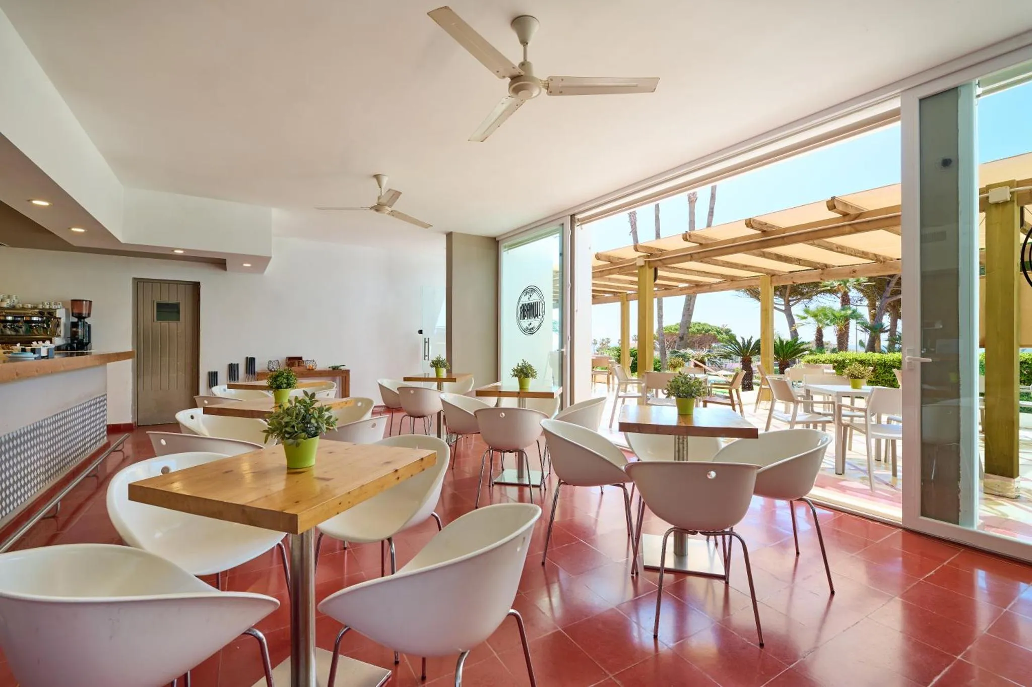 Une salle lumineuse avec des tables et des chaises près d'une ouverture sur une terrasse ombragée.