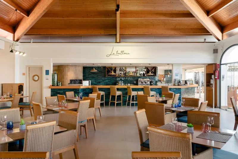 Une salle de restaurant lumineuse avec un bar et des tables disposées sur un sol carrelé.