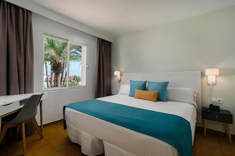 Une chambre lumineuse avec un grand lit et une fenêtre donnant sur la végétation.