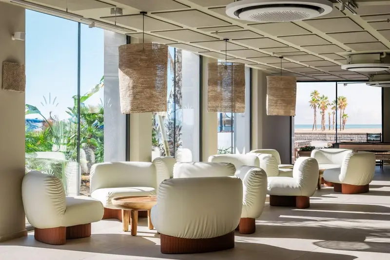 Espace de détente intérieur avec canapés et luminaires suspendus face à une vue sur la mer.