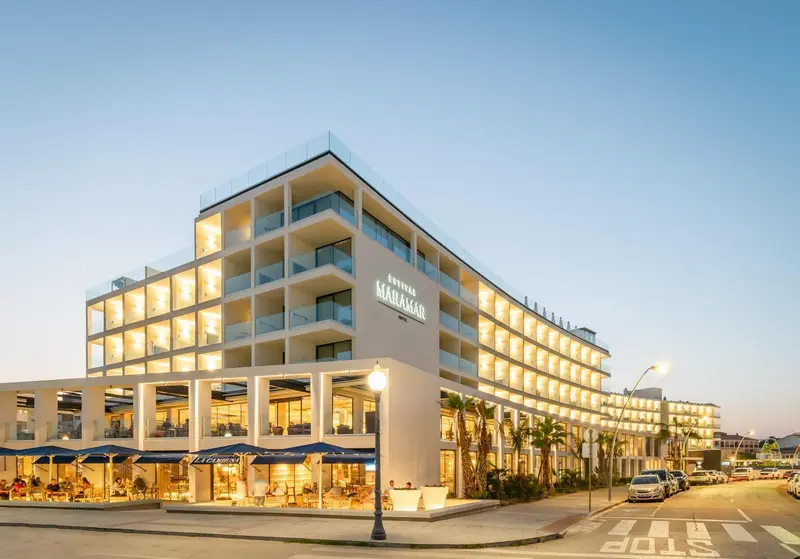 Bâtiment moderne à plusieurs étages avec des balcons illuminés et une façade blanche.