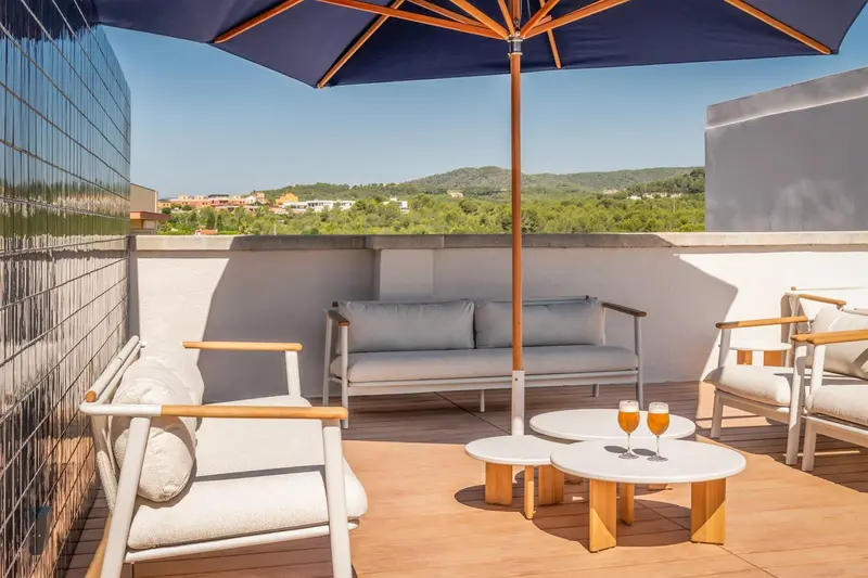 Terrasse aménagée avec canapé, fauteuils et tables basses offrant une vue sur le paysage.