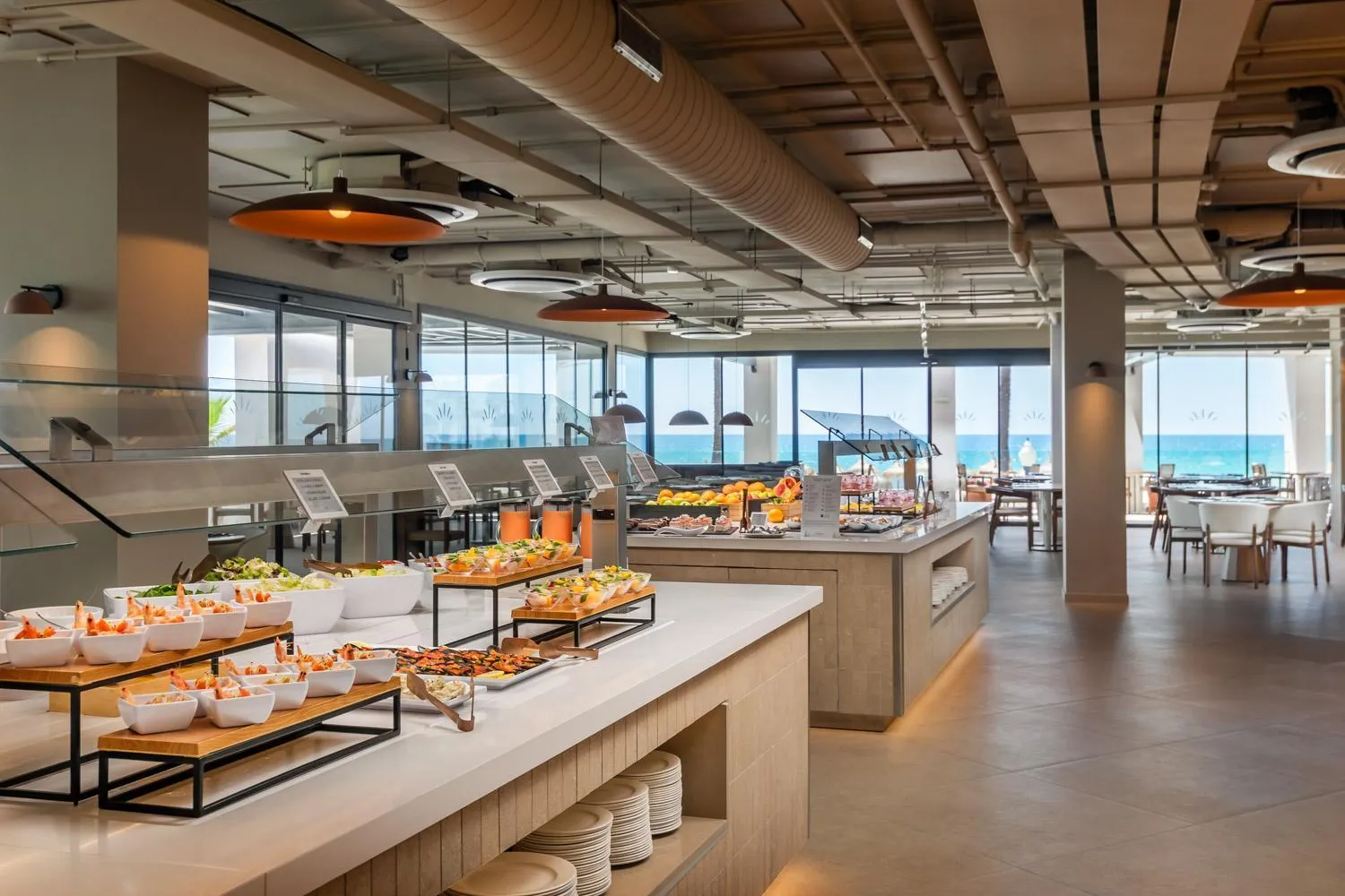Un buffet propose une variété de plats frais et colorés dans une salle lumineuse avec vue sur la mer.