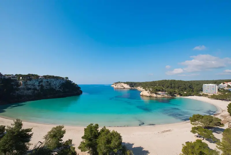Une plage de sable fin bordée d'une eau turquoise et de falaises verdoyantes.
