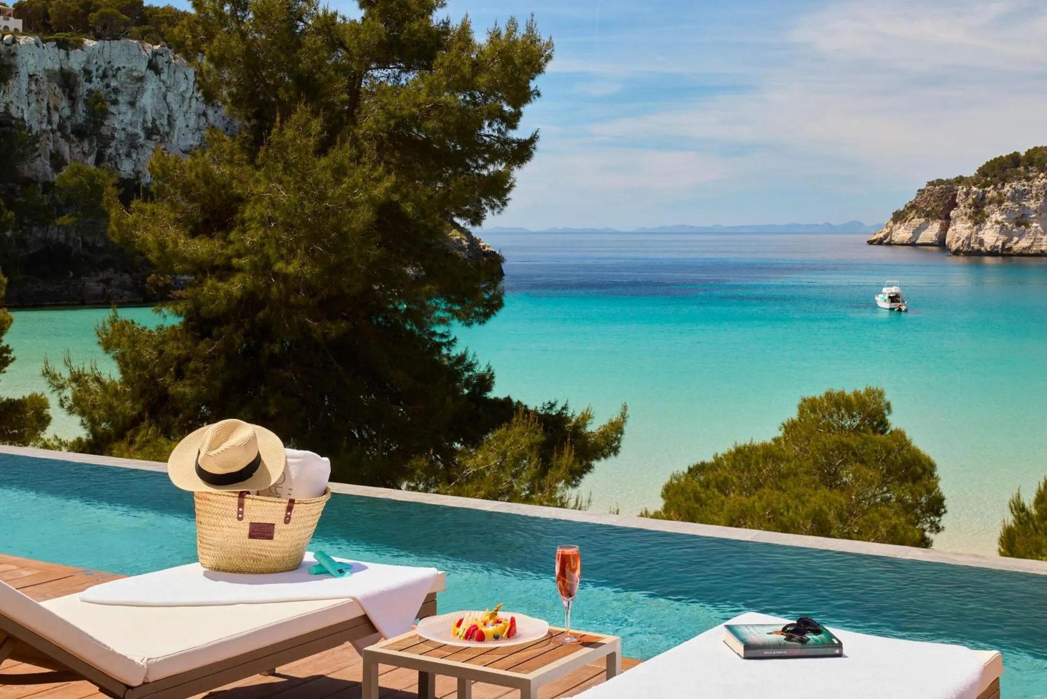 Deux transats avec un chapeau et des serviettes au bord d'une piscine à débordement, avec vue sur la mer.