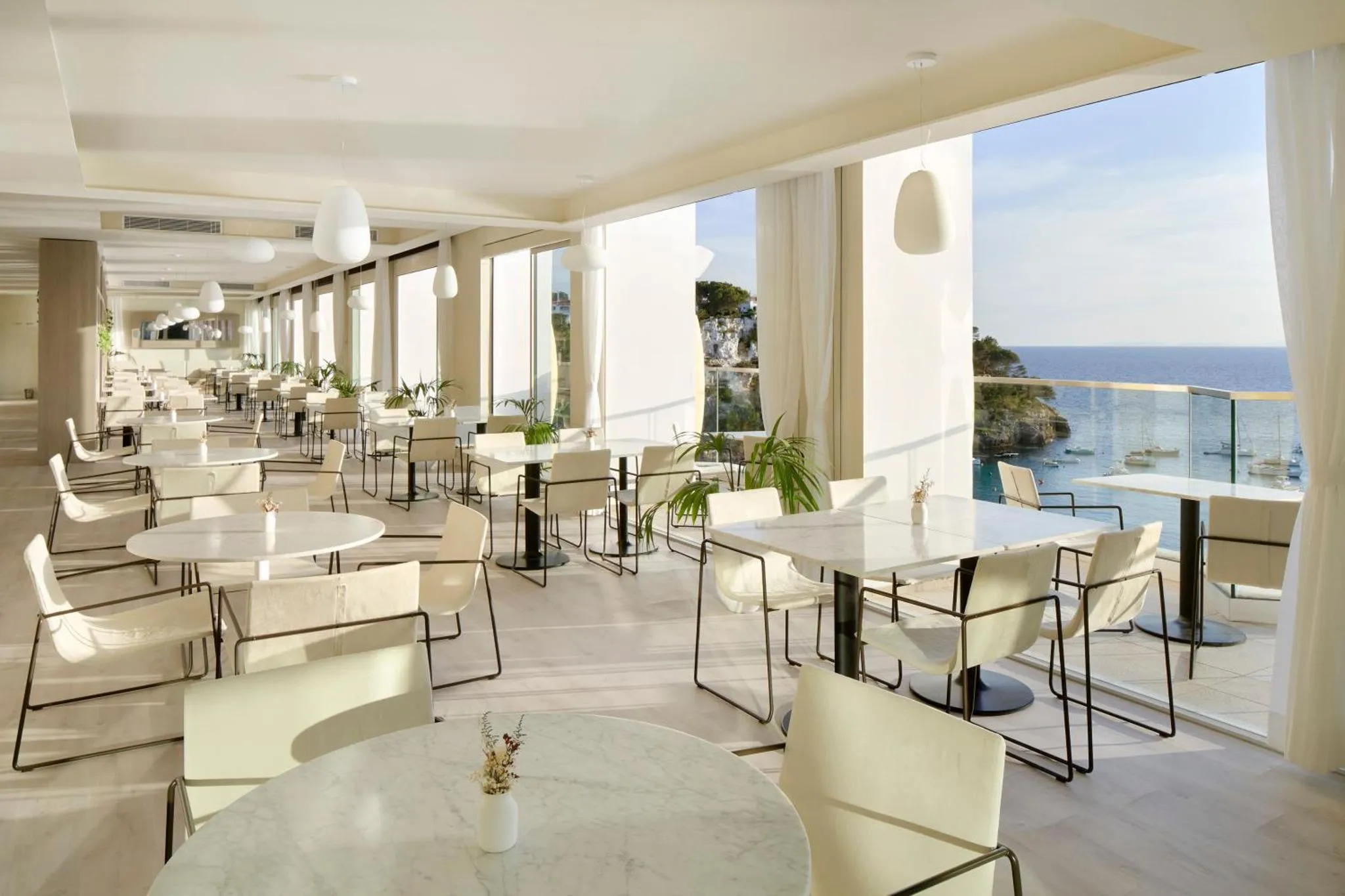 Une salle lumineuse avec des tables et des chaises près de grandes fenêtres donnant sur la mer.