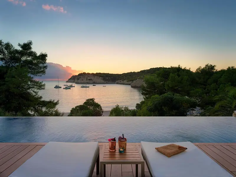 Vue sur une baie au coucher du soleil depuis une piscine à débordement.