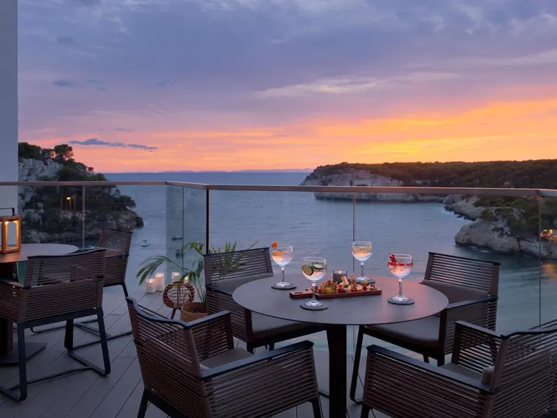 Une table est dressée sur une terrasse avec vue sur la mer au coucher du soleil.