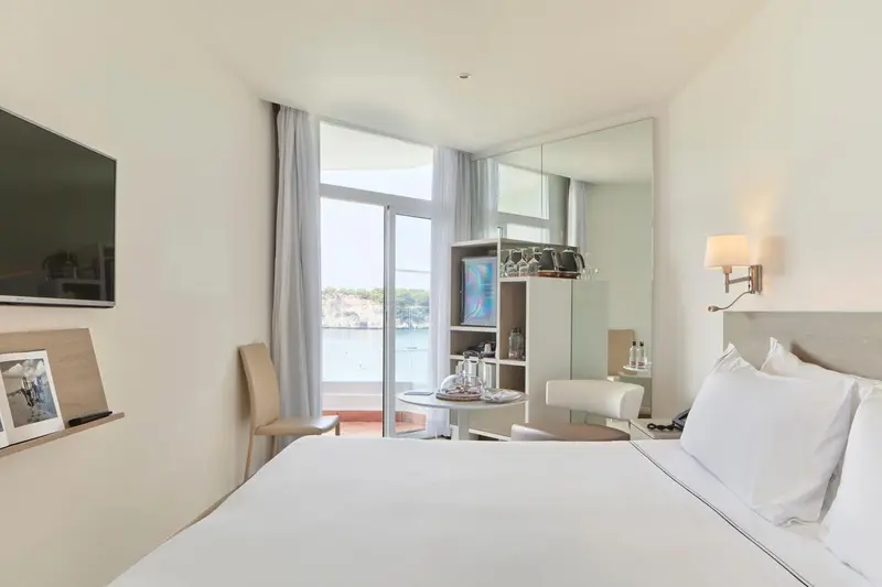 Chambre lumineuse avec un lit blanc et une vue sur la mer.