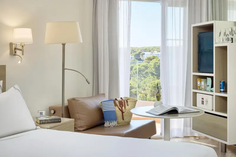 Une chambre lumineuse avec un lit blanc et un coin lecture près d'une fenêtre.