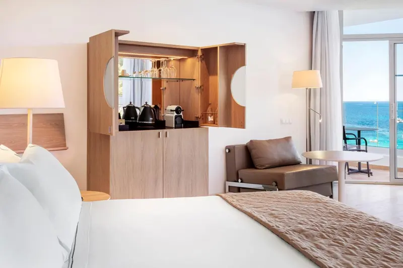 Une chambre lumineuse avec un lit, un coin salon et une vue sur la mer.