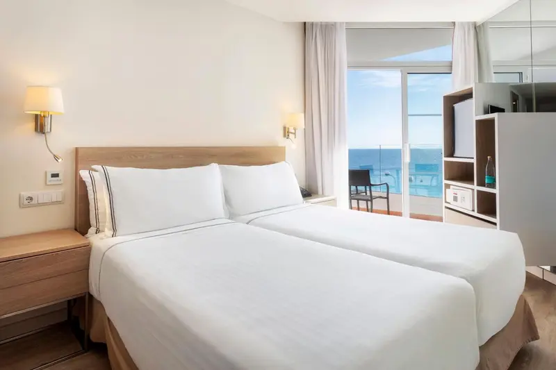Une chambre lumineuse avec un grand lit donnant sur une vue mer.