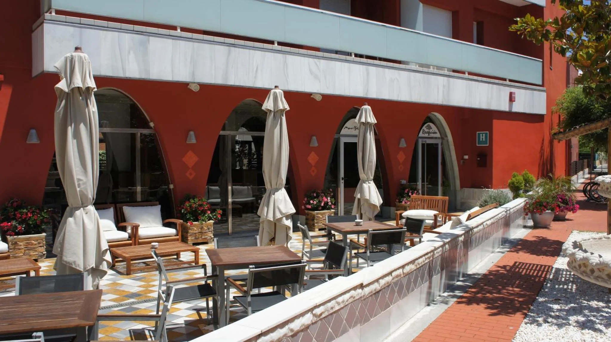Terrasse ombragée avec tables et chaises devant un bâtiment rouge et blanc.
