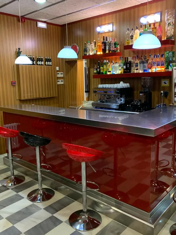 Un comptoir de bar rouge avec des tabourets et des bouteilles exposées sur des étagères.