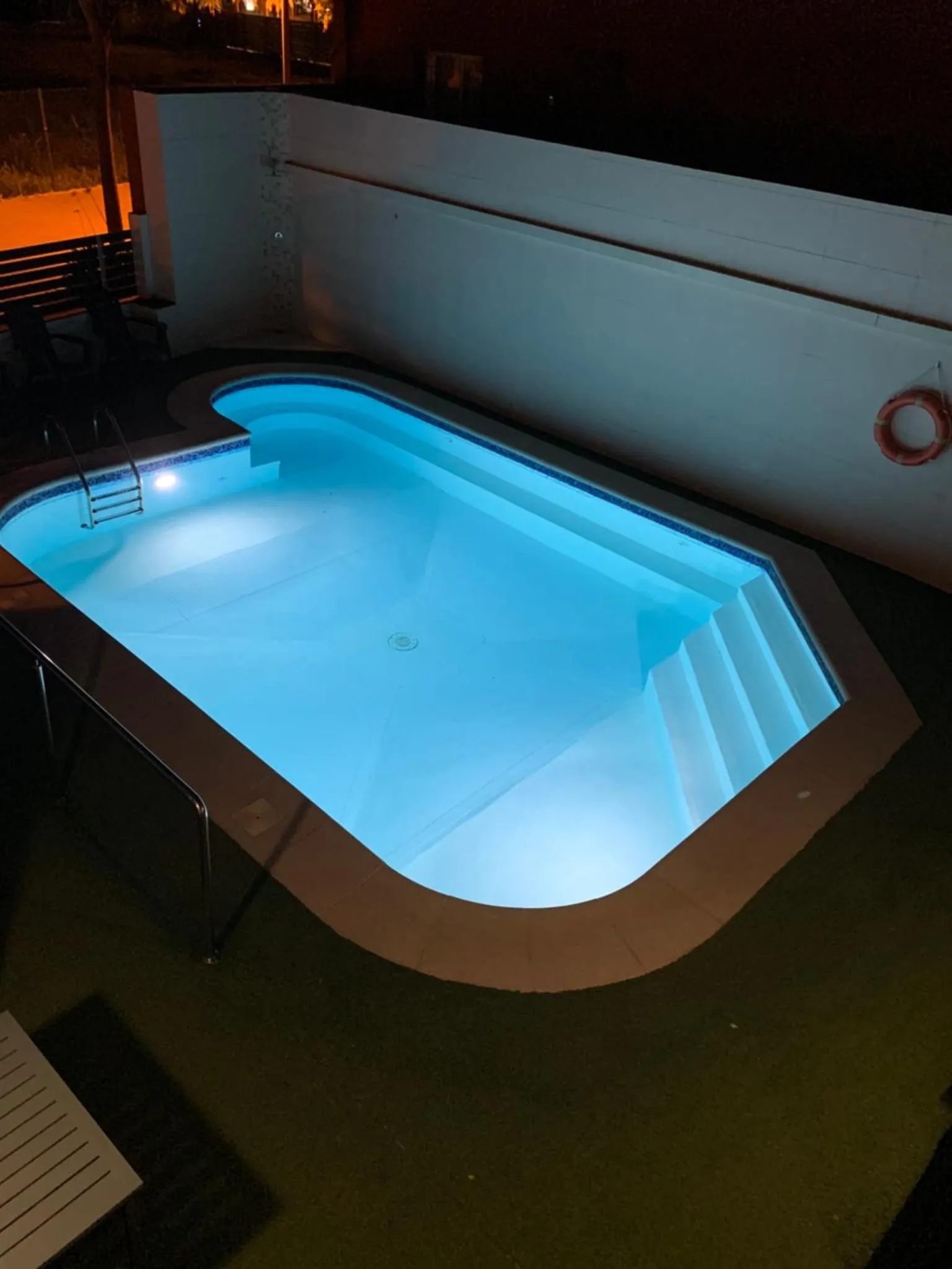 Piscine illuminée avec escalier d'accès et bordure sombre.